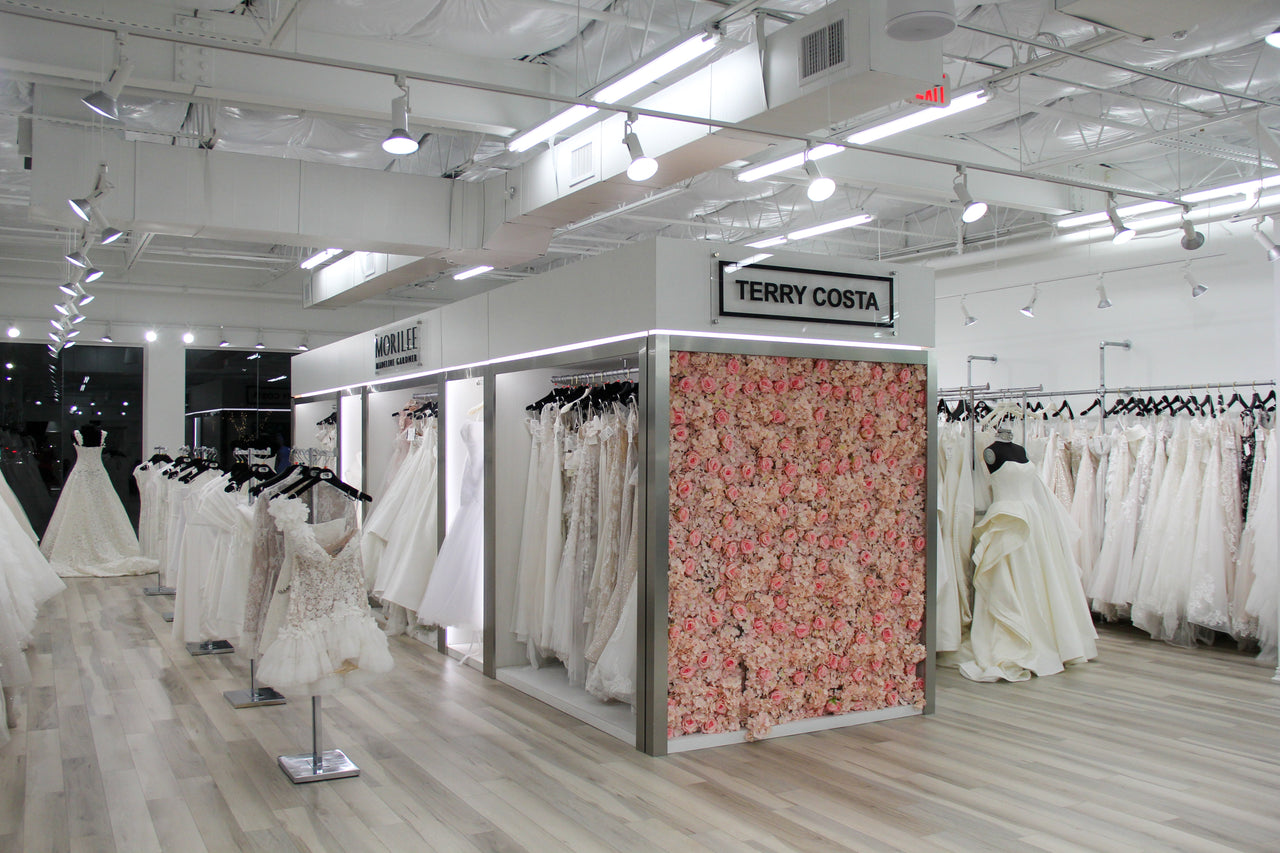 Bridal boutique at Terry Costa featuring racks of wedding dresses, designer gowns, and a floral display wall.